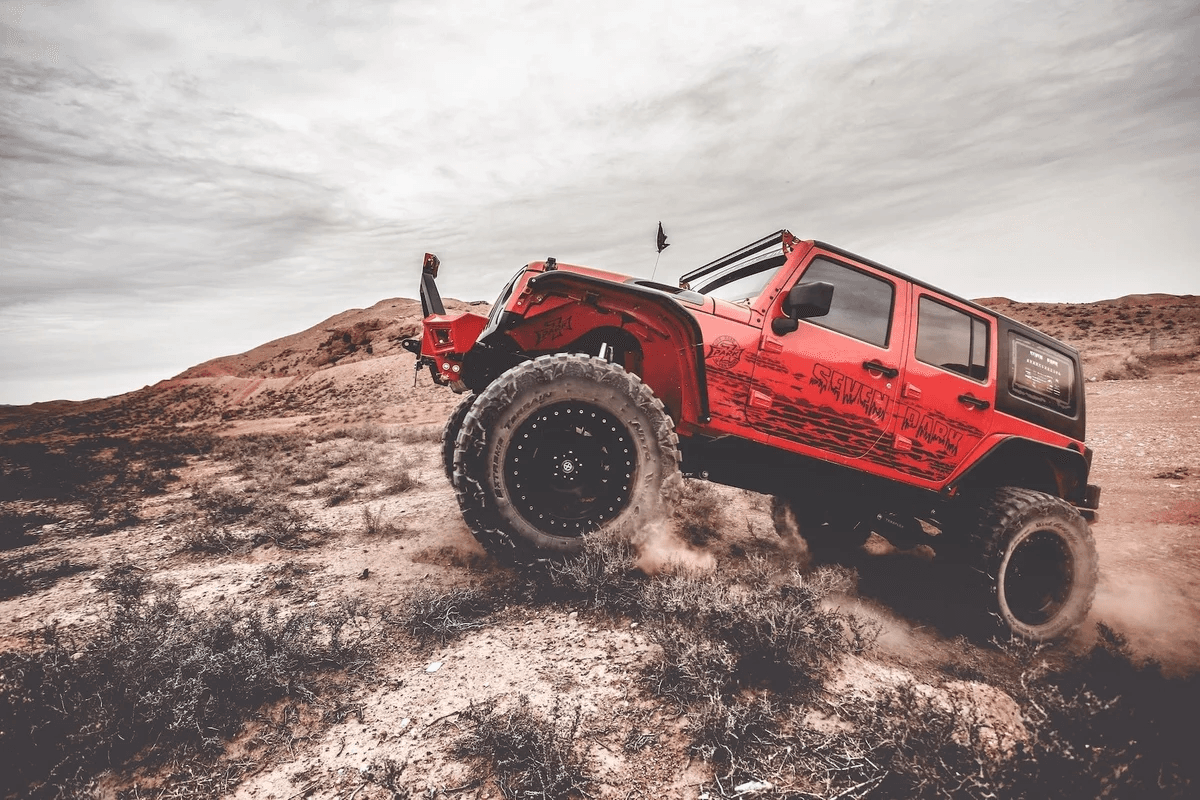 Red off-road Jeep climbing through rugged desert terrain